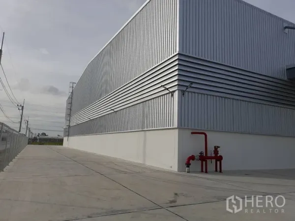 Factory for rent in Mueang Rayong, Rayong - Side elevation of metal-paneled factory showing spacious truck driveway and visible fire safety pipes.