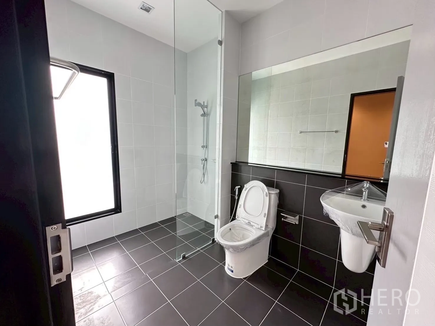 Home Office for rent in Lat Phrao, Bangkok - Bright bathroom with glass shower partition, large mirror, and black-and-white tiles.