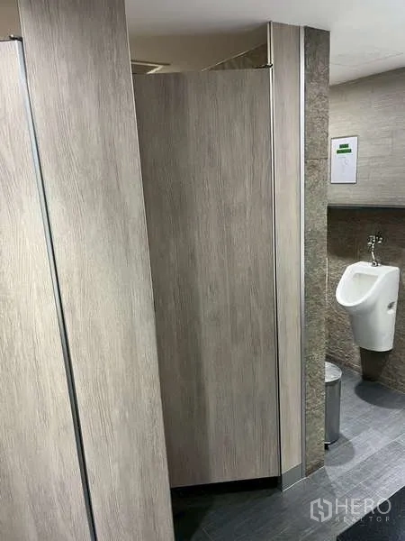 Office Space for rent - Men’s restroom with partitioned stalls and a wall-mounted urinal.