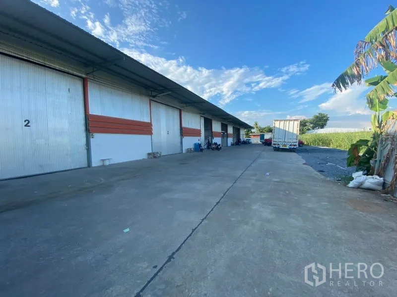 Warehouse for rent in Mueang Pathum Thani, Pathum Thani - Expansive concrete loading area beside warehouse units providing truck access and turning space.