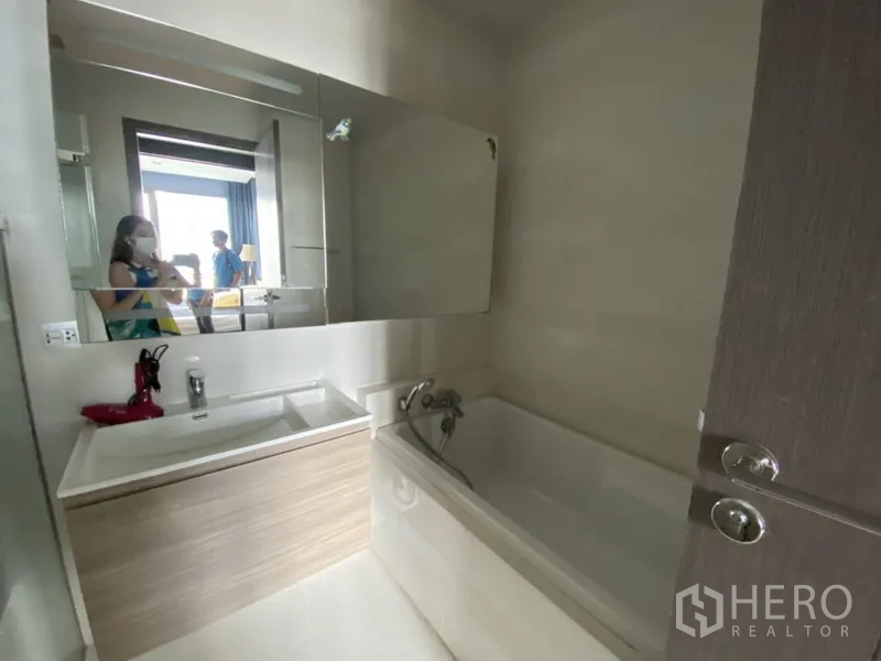 Condominium for rent in Khlong Toei, Bangkok - Bathroom featuring a white bathtub, wide mirror and modern sink cabinet