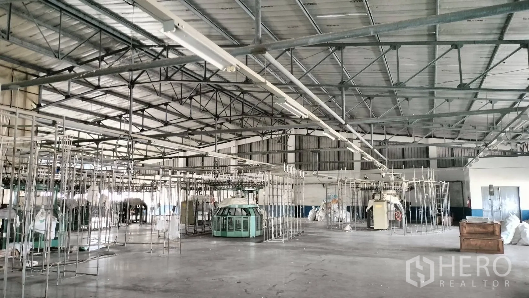 Factory for rent in Lat Krabang, Bangkok - Steel truss roof with suspended lighting above a wide manufacturing floor and machinery frames.