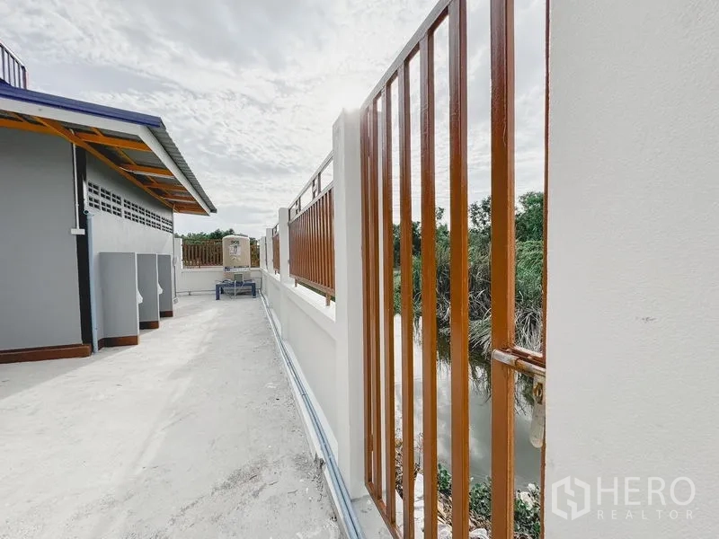 Warehouse for rent or sale in Khlong Luang, Pathum Thani - Perimeter fence with wood-tone vertical slats overlooking a canal beside the site.