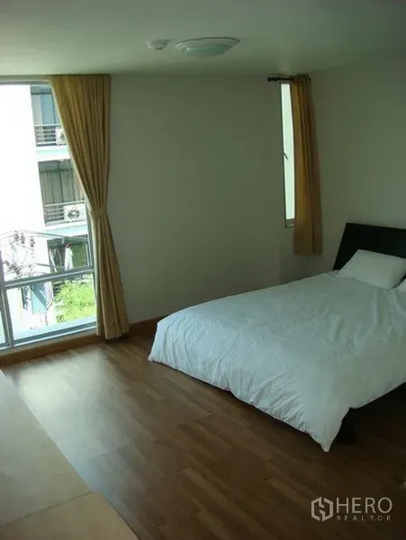 Apartment for rent in Khlong Toei, Bangkok - Spacious bedroom with double bed, floor-to-ceiling windows and curtains.