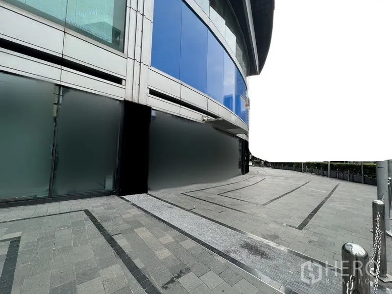 Retail Space for rent - Curved glass retail façade with frosted lower panels and a wide paved walkway at a modern commercial building.