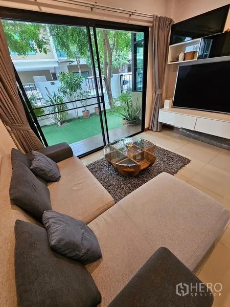 Detached House for rent in Bang Phli, Samut Prakan - Living room with L-shaped sofa, sliding glass doors to the garden and TV unit.