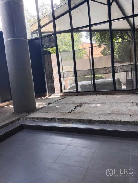 Retail Space for rent in Watthana, Bangkok - Double-height retail shell with floor-to-ceiling glass frontage and concrete floor facing greenery.