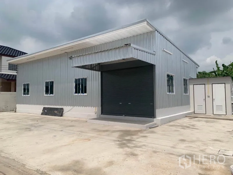 Warehouse for rent or sale in Thanyaburi, Pathum Thani - Warehouse exterior featuring large roller shutter door and ample driveway.