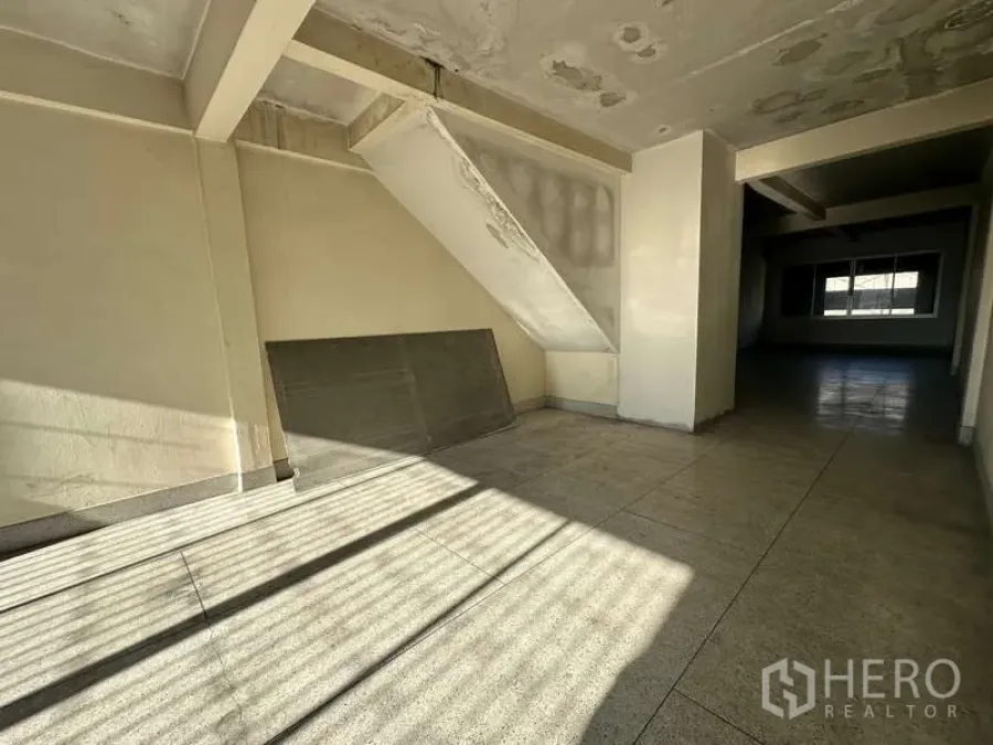 Office Space for rent in Phra Khanong, Bangkok - Sunlit empty office interior with tiled floors, an under-stair nook, and a deep open-plan area leading to a windowed workspace.