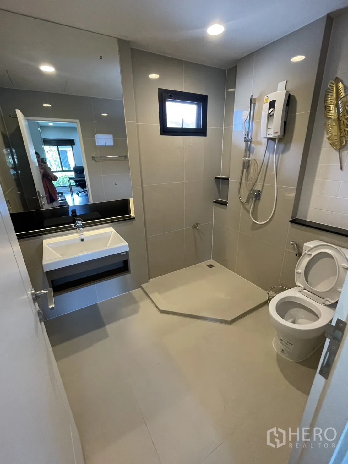 Detached House for rent or sale in Lam Luk Ka, Pathum Thani - Contemporary bathroom with walk-in shower, wall-mounted sink, large mirror and toilet in gray tiles.