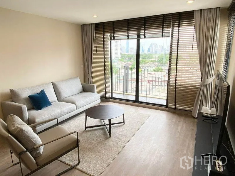 Condominium for rent in Pathum Wan, Bangkok - Living area from another angle with large sliding doors, rug and skyline view beyond the balcony.