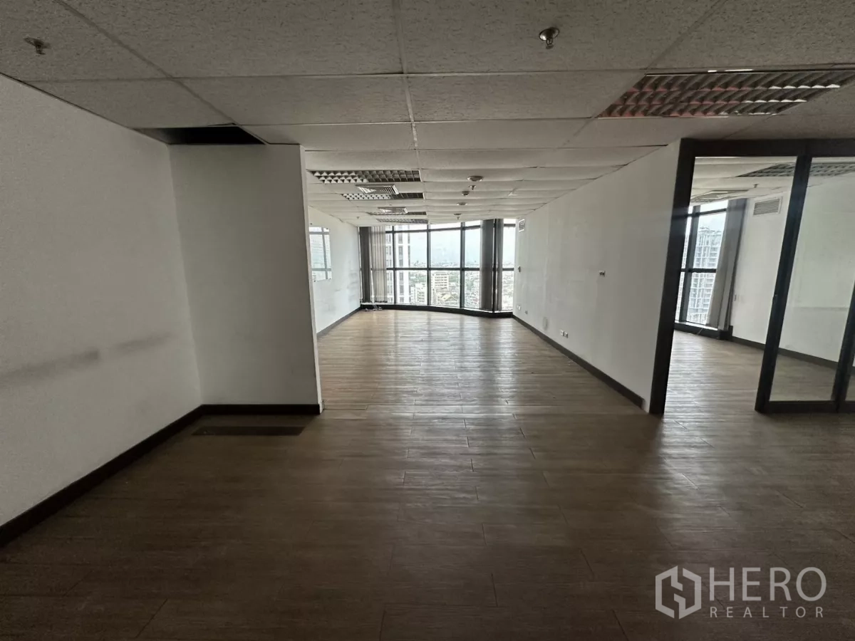 Office Space for rent in Watthana, Bangkok - Long open workspace with white walls, suspended ceiling lighting, and large windows at the end bringing in natural light.