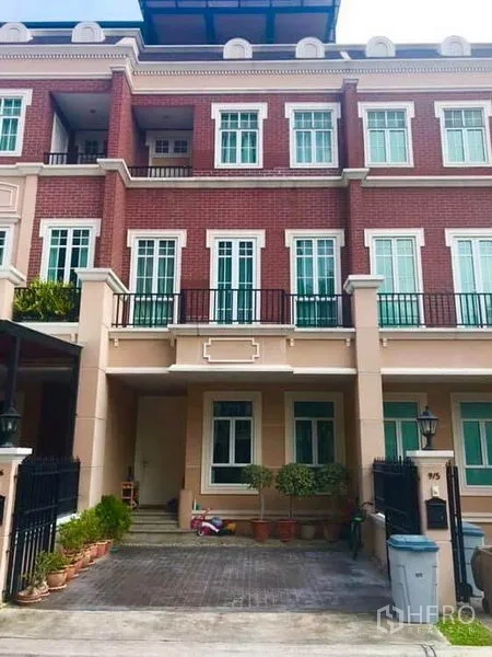 Townhouse for rent or sale in Bangkok - Three-storey townhouse in Watthana, Bangkok with red-brick facade, balconies and gated driveway.
