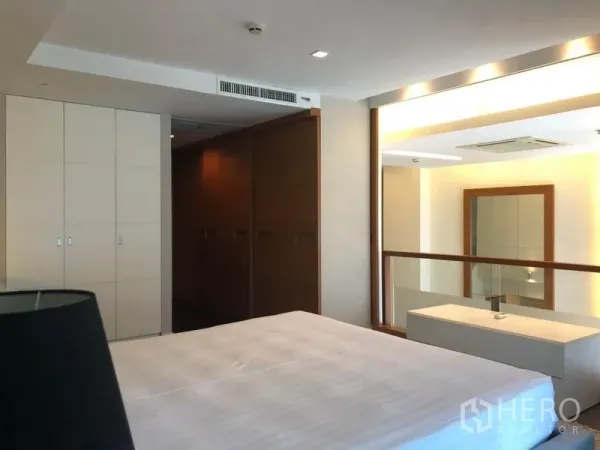 Condominium for rent in Pathum Wan, Bangkok - Master bedroom with built-in wardrobes and a glass partition overlooking the living area.
