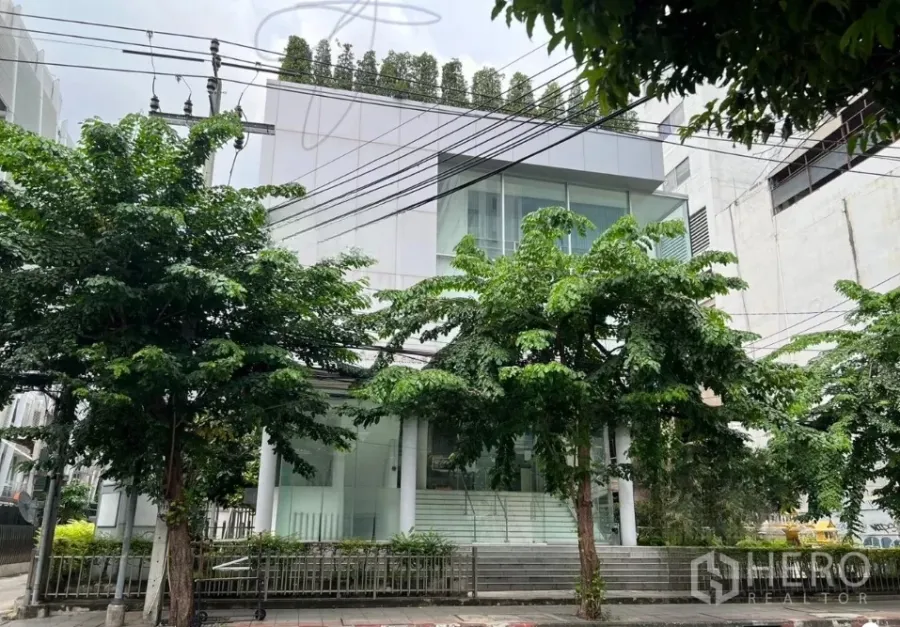 Office Space for rent in Bang Rak, Bangkok - Modern glass-front office building on a tree-lined street in Bangkok.