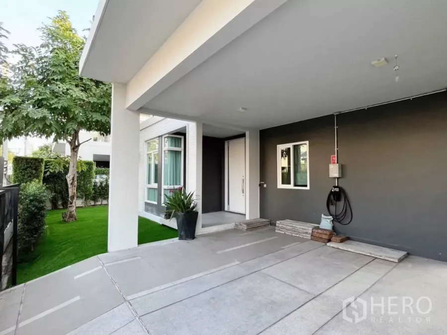 Detached House for rent in Samut Prakan - Covered carport with EV charging point beside the front garden of a modern detached house.