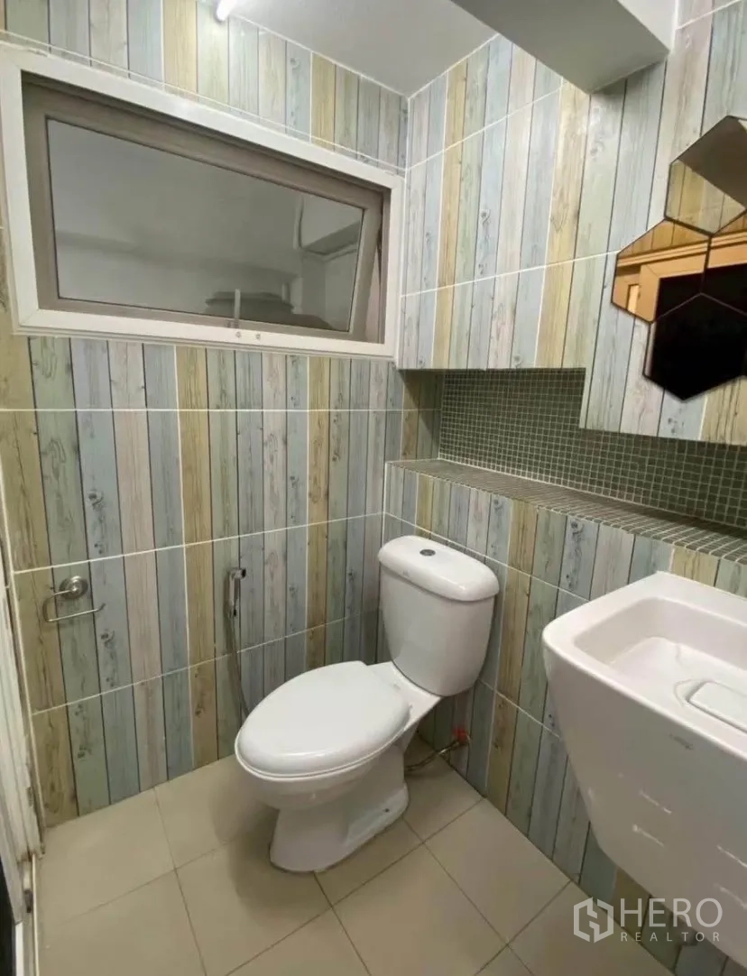 Townhouse for rent in Phra Khanong, Bangkok - Compact bathroom with vertical wood-look tiles, window, toilet, and wall sink.