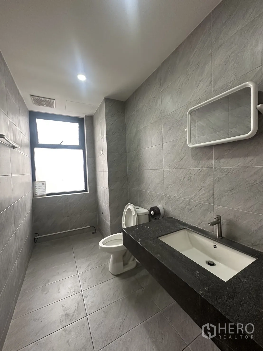 Home Office for rent in Pathum Wan, Bangkok - Modern bathroom with gray tiles, a black countertop basin and toilet by a window.