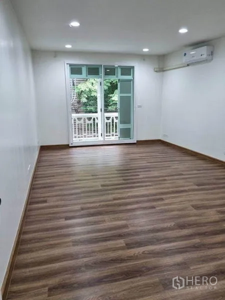 Shophouse for rent in Bang Rak, Bangkok - Bedroom with laminate floor, sliding glass door to a small balcony and wall-mounted air conditioner.
