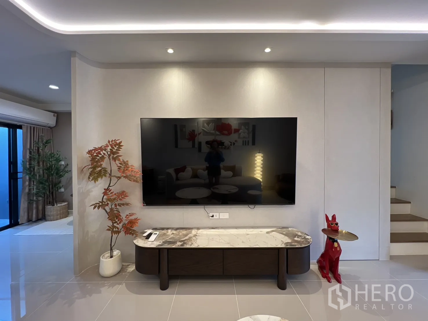 Townhouse for rent in Bang Phli, Samut Prakan - Living room feature wall with mounted TV, marble console, recessed lighting and nearby stairs.