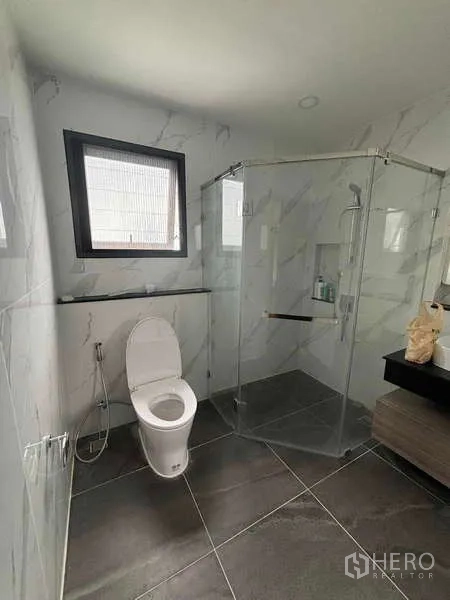 Detached House for rent in Mueang Nonthaburi, Nonthaburi - Bright bathroom featuring a glass shower enclosure, toilet and marble-look wall tiles.