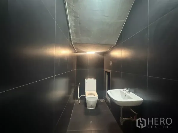 Home Office for rent in Pathum Wan, Bangkok - Bathroom with matte black tiles, toilet and wall-mounted sink under a low ceiling.
