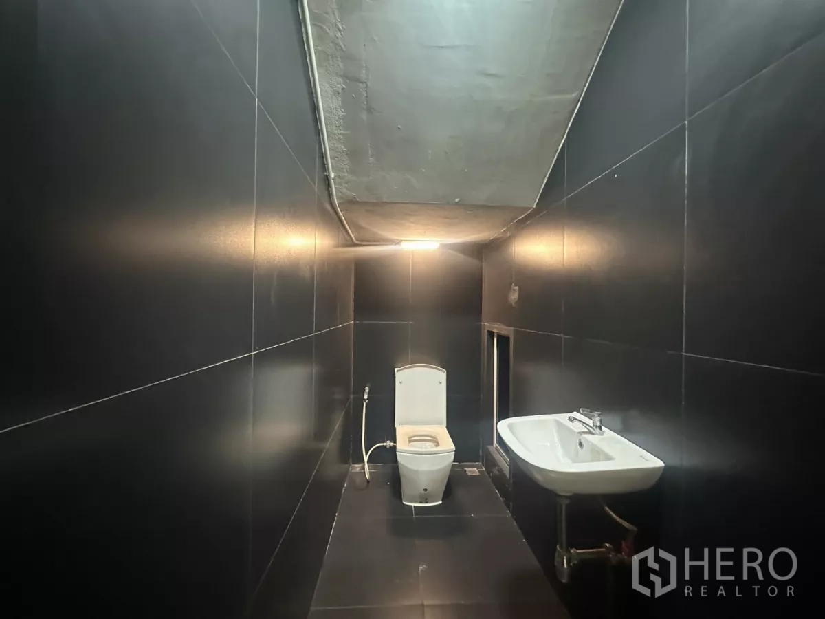 Home Office for rent in Pathum Wan, Bangkok - Bathroom with matte black tiles, toilet and wall-mounted sink under a low ceiling.
