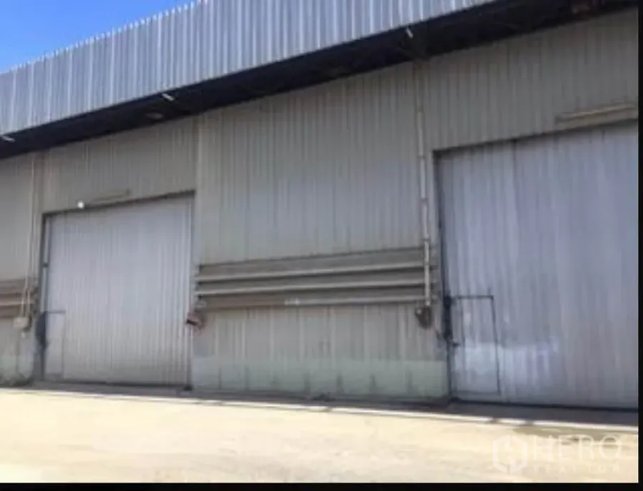 Warehouse for rent in Sai Mai, Bangkok - Corrugated metal warehouse exterior with two large sliding doors and an open concrete loading area under clear sky.