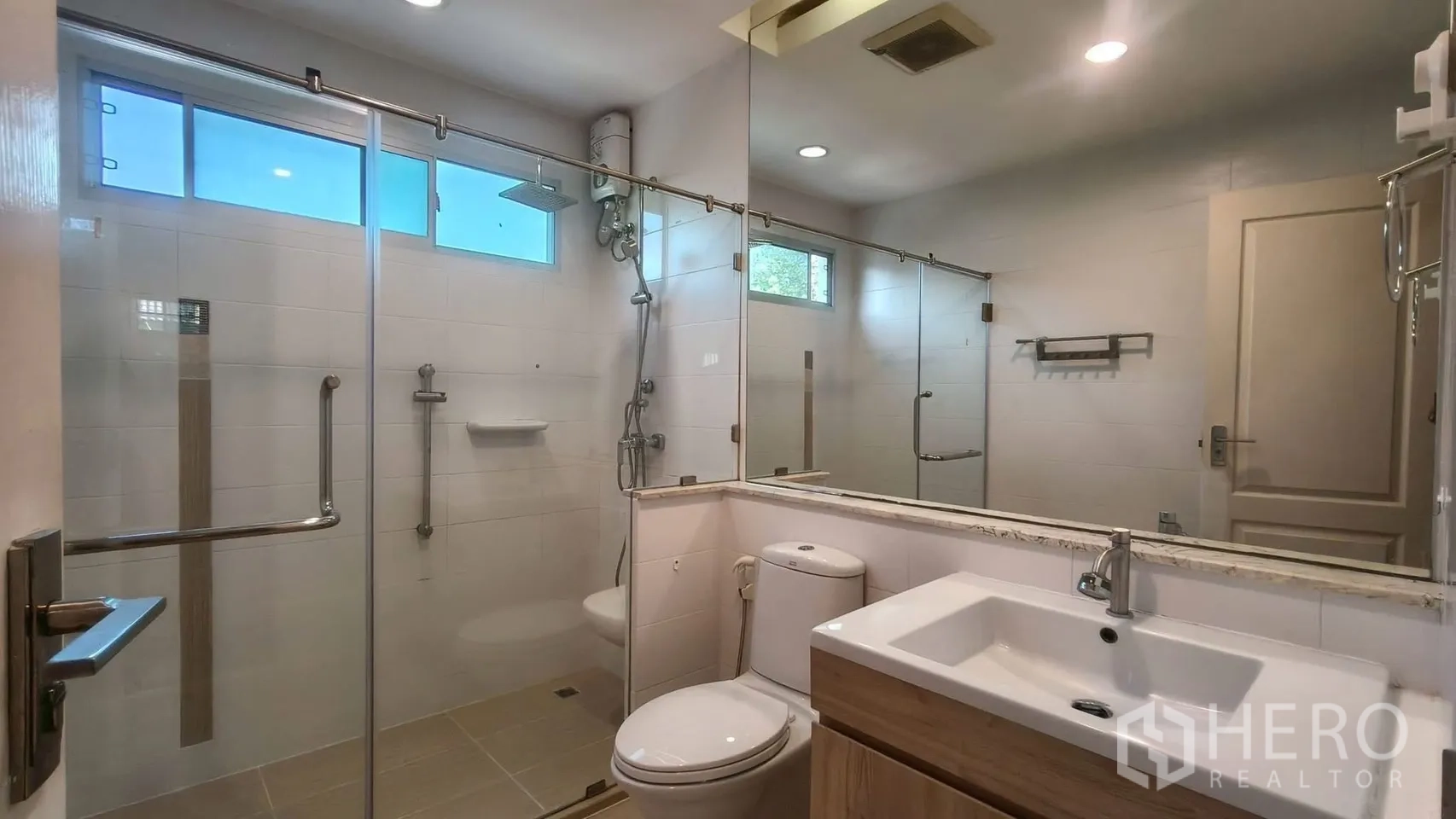 Detached House for rent or sale in Mueang Samut Prakan, Samut Prakan - Modern bathroom with glass-enclosed shower, rain head, handheld spray, wide mirror and vanity.