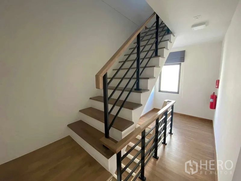 Townhouse for rent in Prawet, Bangkok - Staircase with wooden treads and black metal railings on the upper floor.