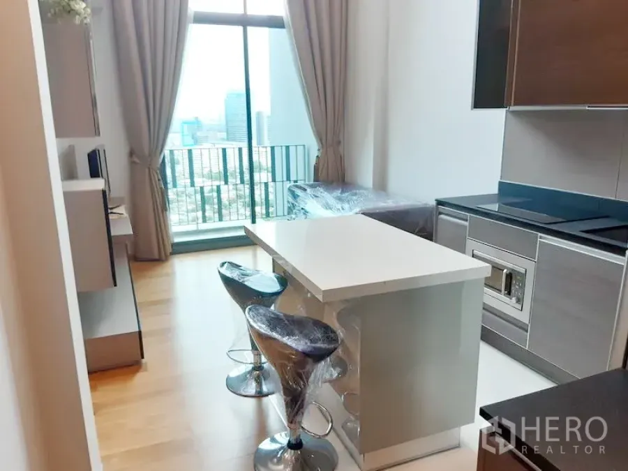 Condominium for rent in Khlong Toei, Bangkok - Bright condo living area with a modern kitchen island and floor-to-ceiling window showing the Bangkok skyline in Khlong Toei.