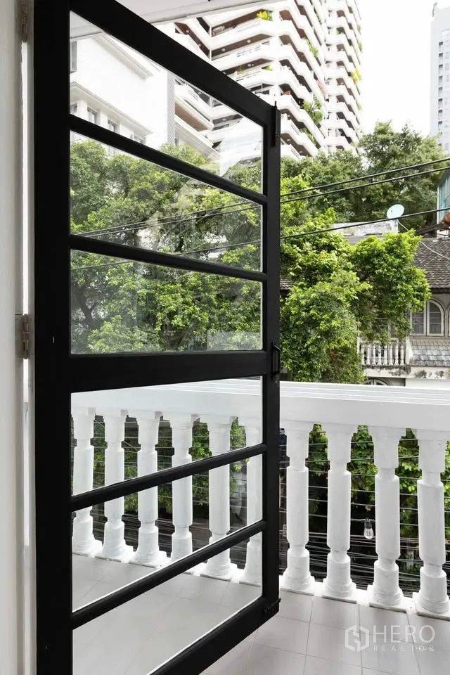 Townhouse for rent in Khlong Toei, Bangkok - Small balcony with white balustrade and black framed door overlooking trees and nearby buildings.