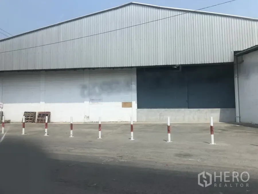 货栈 出租在Nonthaburi - 仓库外立面，带装卸卷帘门、防撞桩与宽阔硬化场地