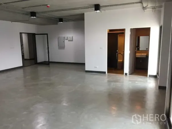 Office Space for rent in Khlong Toei, Bangkok - Spacious office interior showing entrances to the restroom and a glass door, with concrete flooring and exposed ceiling.