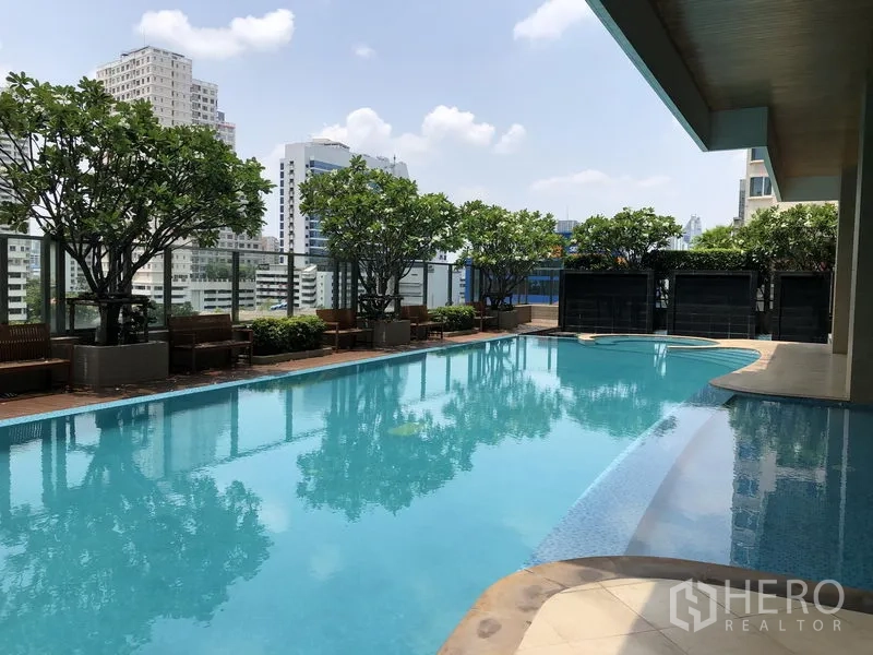 Condominium for rent or sale in Khlong Toei, Bangkok - Rooftop swimming pool with seating, trees and city skyline backdrop.