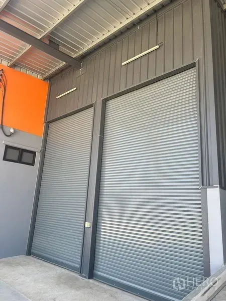 Factory for rent in Bang Pakong, Chachoengsao - Two large metal roller shutter doors beneath a covered loading canopy.