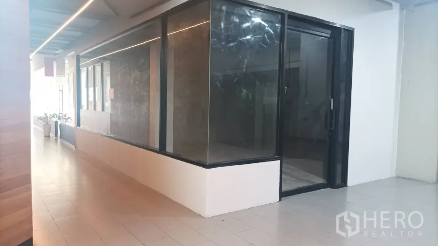 Retail Space for rent - Long indoor corridor with ceiling strip lights facing the shop’s large display windows.