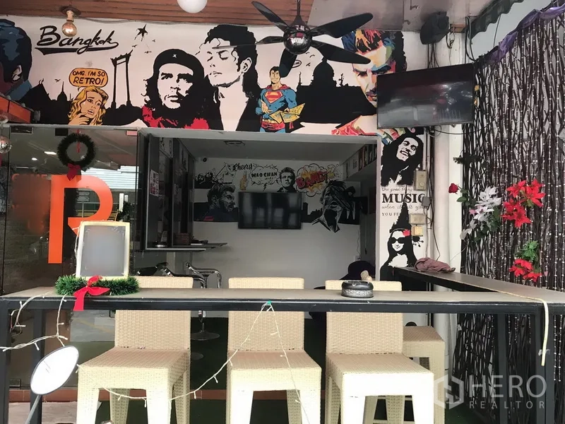 Retail Space for rent in Watthana, Bangkok - Open retail unit featuring rattan bar stools, ceiling fan, wall‑mounted TVs and decorative vines with pop‑art mural backdrop.