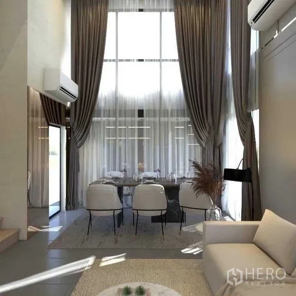 Townhouse for sale in Suan Luang, Bangkok - Double-height dining area with floor-to-ceiling windows and long drapes.