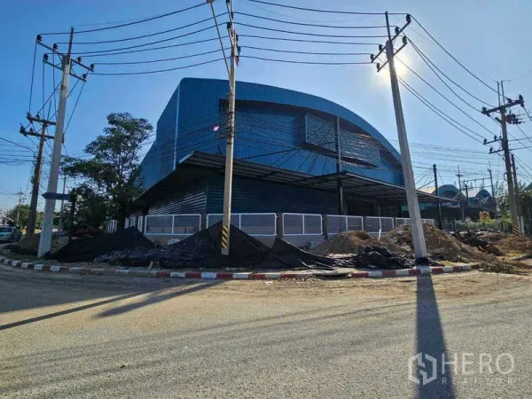 Factory for rent in Chon Buri - Angled exterior of the blue factory showing a loading canopy and roadside power poles.