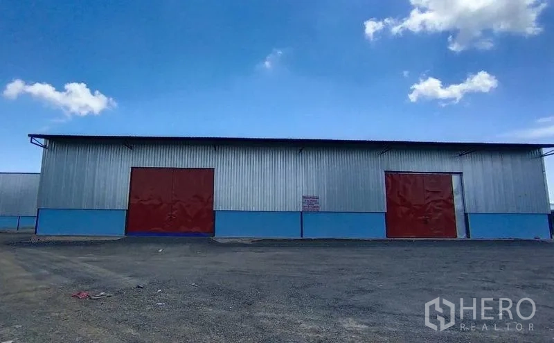 货栈 出租在Si Racha, Chon Buri - 仓库外立面，金属板墙、红色推拉门与宽阔场地
