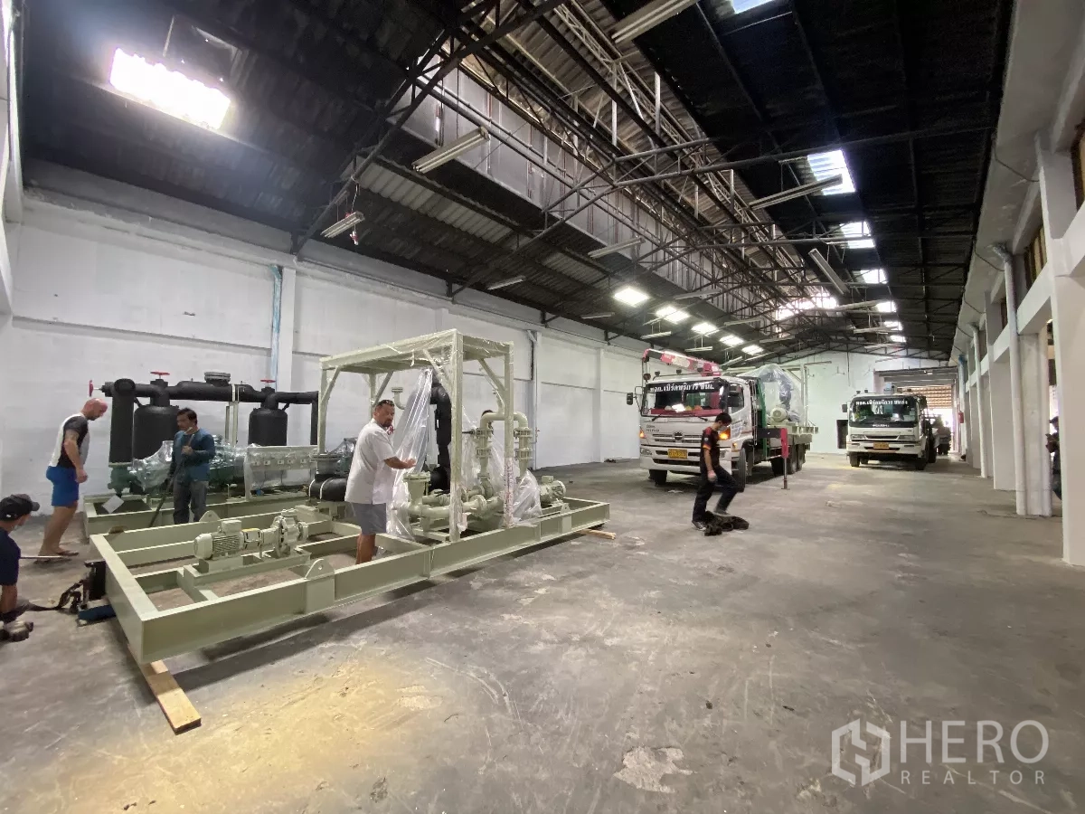 Factory for rent in Bang Phli, Samut Prakan - Long production hall with bright lighting, high truss roof and trucks positioned inside.