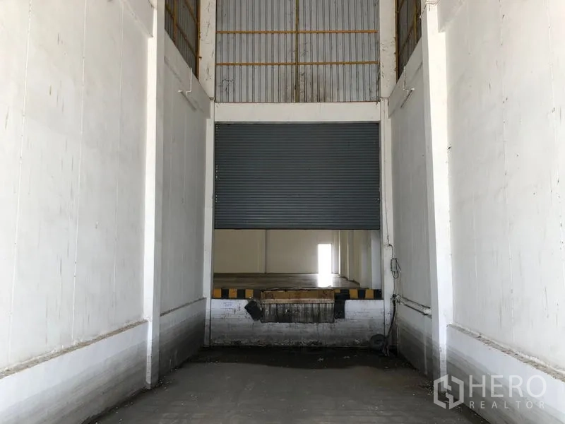 Warehouse for rent in Phra Nakhon Si Ayutthaya - Truck loading bay with half-open shutter and dock bumpers inside the building.