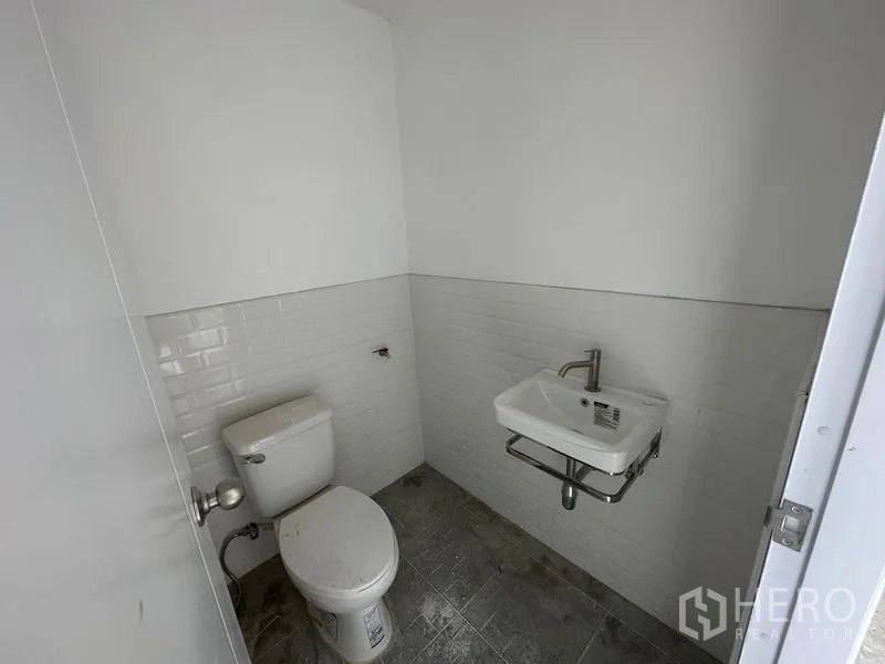 Warehouse for rent in Bang Phli, Samut Prakan - Compact restroom with white wall tiles, a wall-mounted sink and a toilet inside the warehouse.
