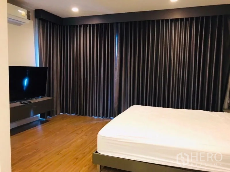 Detached House for rent or sale in Pathum Thani - Master bedroom with wood floors, bed and blackout curtains.
