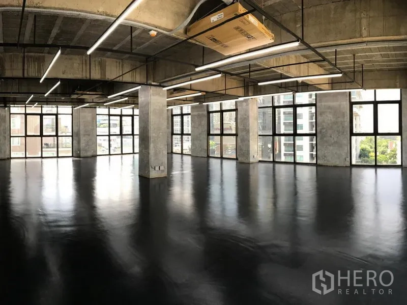 Office Space for rent in Khlong Toei, Bangkok - Open-plan industrial office with exposed concrete ceiling, black polished floors, and large grid windows with city views.