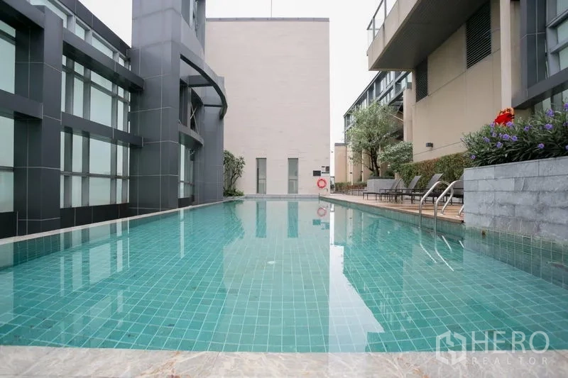 Condominium for rent or sale in Pathum Wan, Bangkok - Outdoor lap pool with turquoise tiles, sun loungers and landscaped deck between modern buildings.