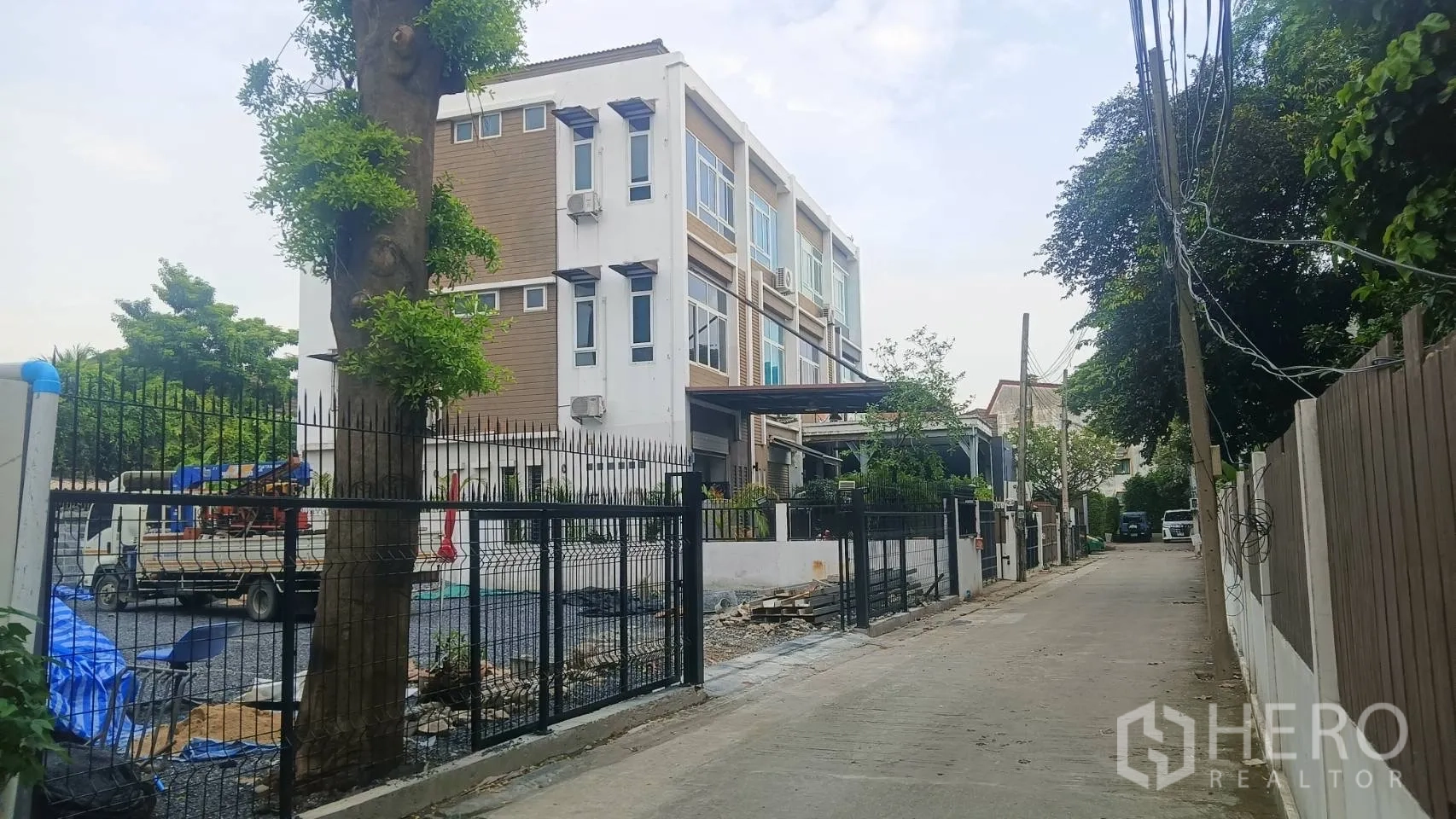 Home Office for rent in Wang Thonglang, Bangkok - Street view of modern four-storey corner home office with black perimeter fence and side parking area.