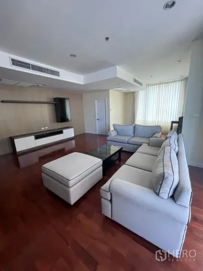 Condominium for rent in Khlong Toei, Bangkok - Spacious living room featuring sectional sofas, ottoman, media wall and polished hardwood floors.