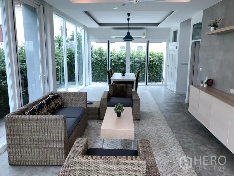 独立式住宅 出租或出售在Huai Khwang, Bangkok - 采光充足的客餐厅，一体化布局，藤制沙发，落地玻璃望向绿篱花园